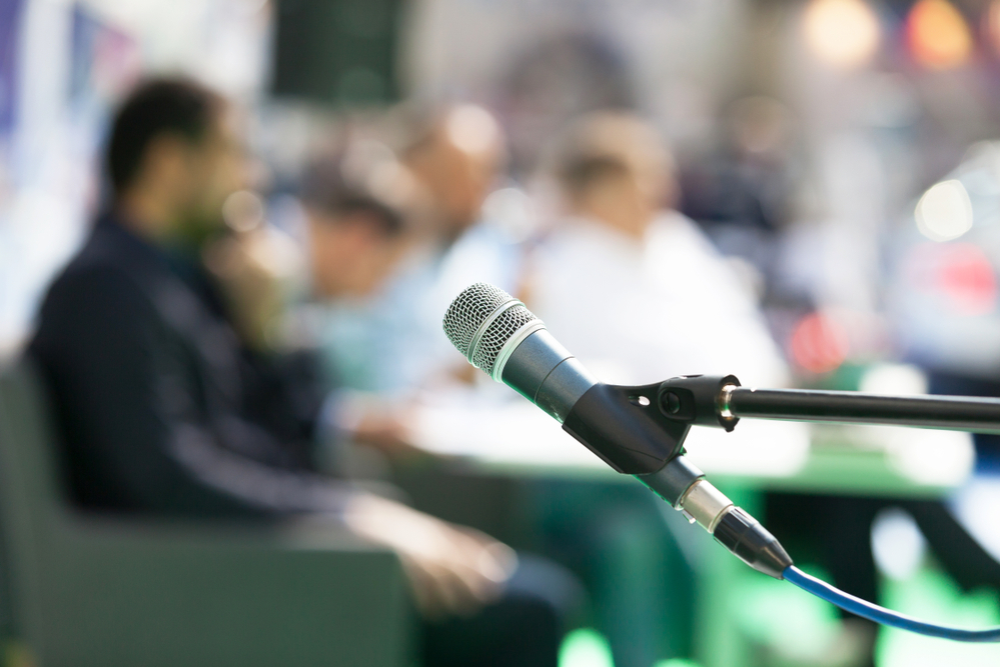 Microphone in focus with blurred people at roundtable event in the background